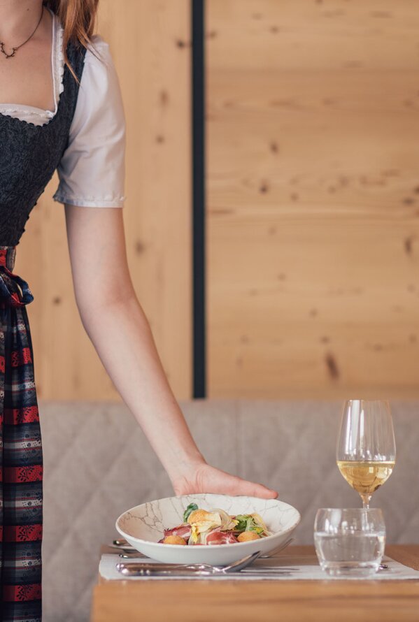Eine Frau im Dirndl serviert ein Gericht an einem gedeckten Tisch im Restaurant.