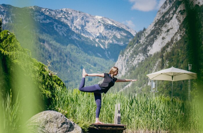 Frau macht Yoga auf Felsen im See, Spiegelung im Wasser, Berge im Hintergrund