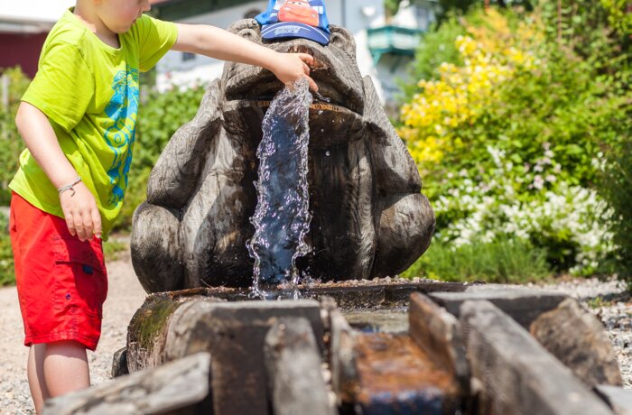 Junge spielt mit Wasser an einem hölzernen Brunnen in Froschform