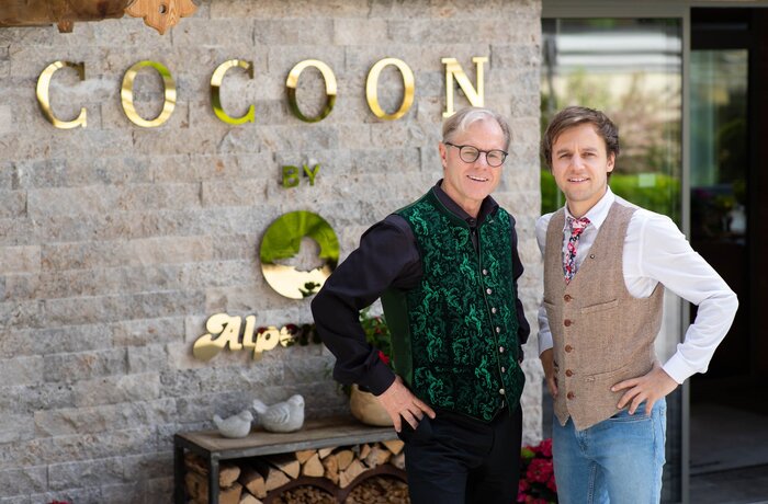 Wolfgang Kostenzer sen. & Wolfgang Kostenzer jun. vor einer Wand mit dem Schriftzug Cocoon by Alpenrose