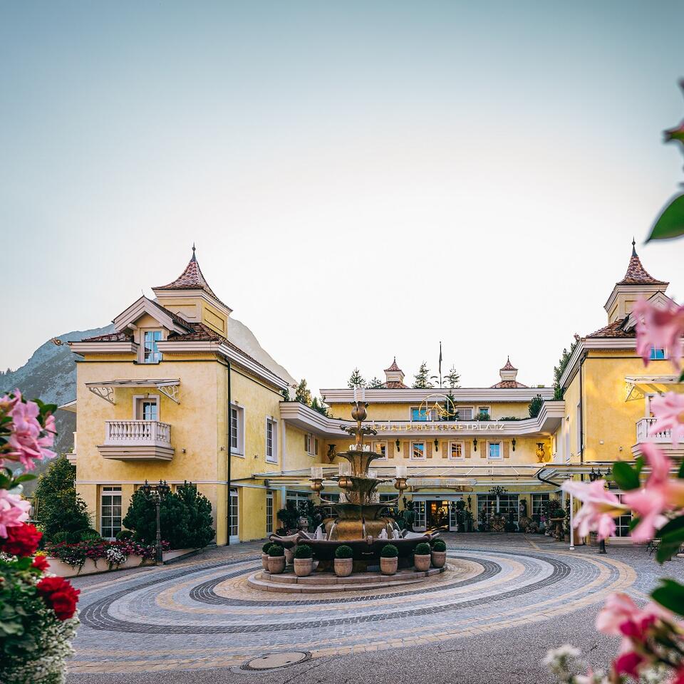 Gelbes Hotelgebäude mit Brunnen im Vordergrund, umrahmt von rosa Blüten