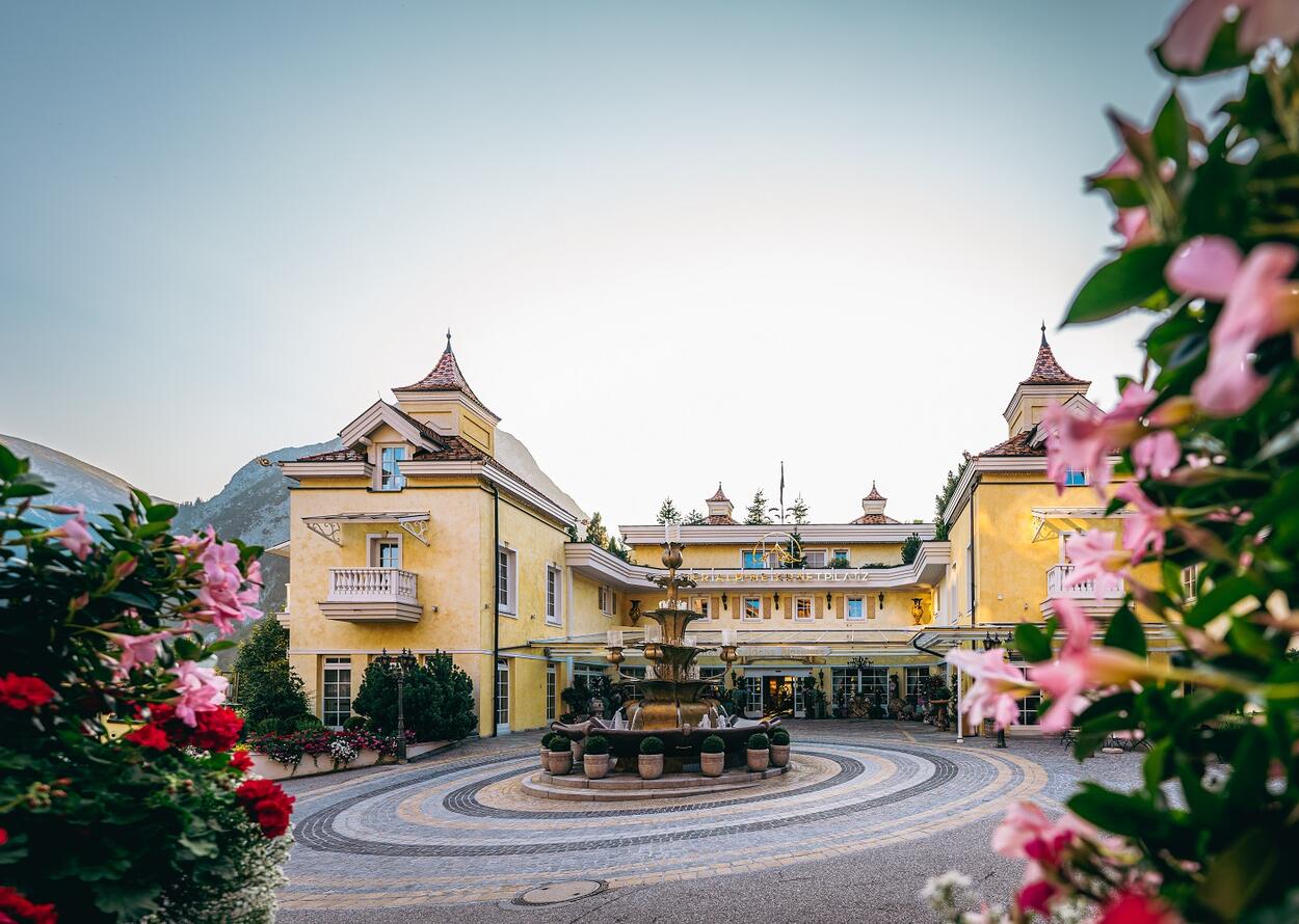 Yellow hotel building with fountain in the foreground, framed by pink flowers