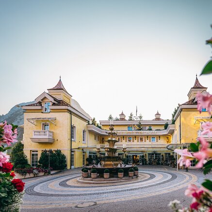 Gelbes Hotelgebäude mit Brunnen im Vordergrund, umrahmt von rosa Blüten