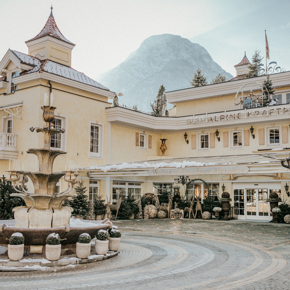 Elegante Hotelaußenansicht mit historischem Charme, Brunnen und Bergkulisse im Winter