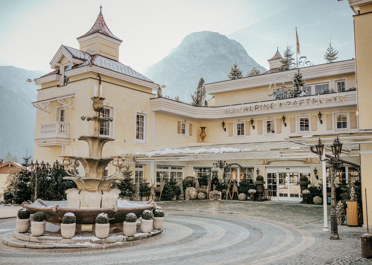 Elegant hotel exterior with historic charm, fountain, and mountain backdrop in winter
