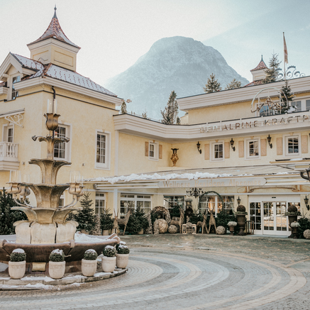 Elegante Hotelaußenansicht mit historischem Charme, Brunnen und Bergkulisse im Winter