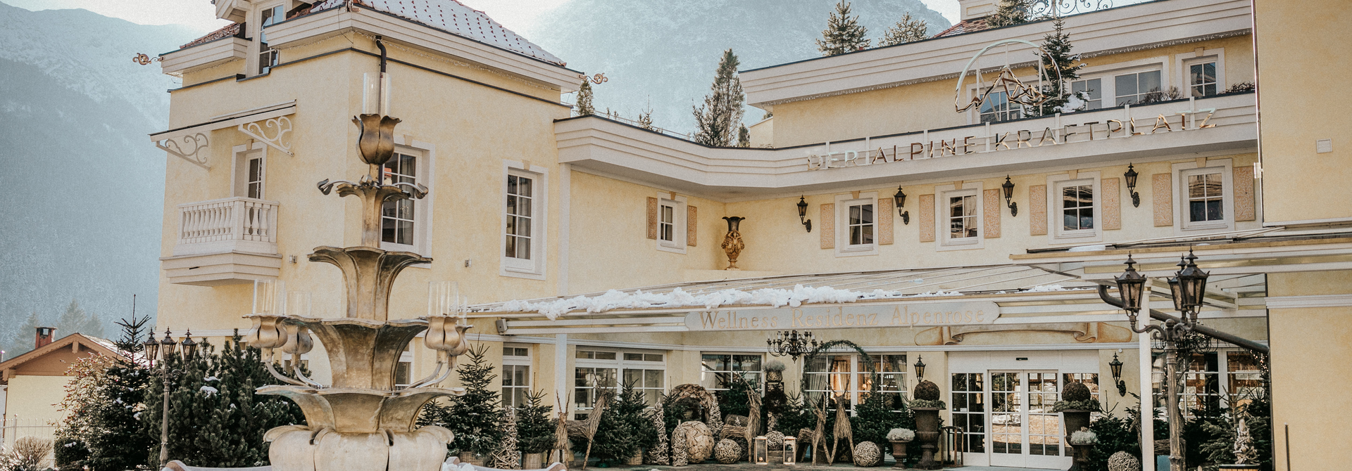 Elegante Hotelaußenansicht mit historischem Charme, Brunnen und Bergkulisse im Winter