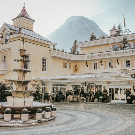 Elegant hotel exterior with historic charm, fountain, and mountain backdrop in winter