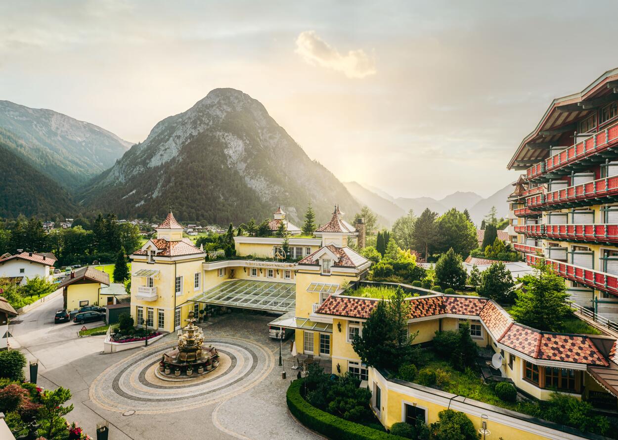 Elegante Hotelanlage mit Brunnen, alpiner Architektur und Bergpanorama im Abendlicht