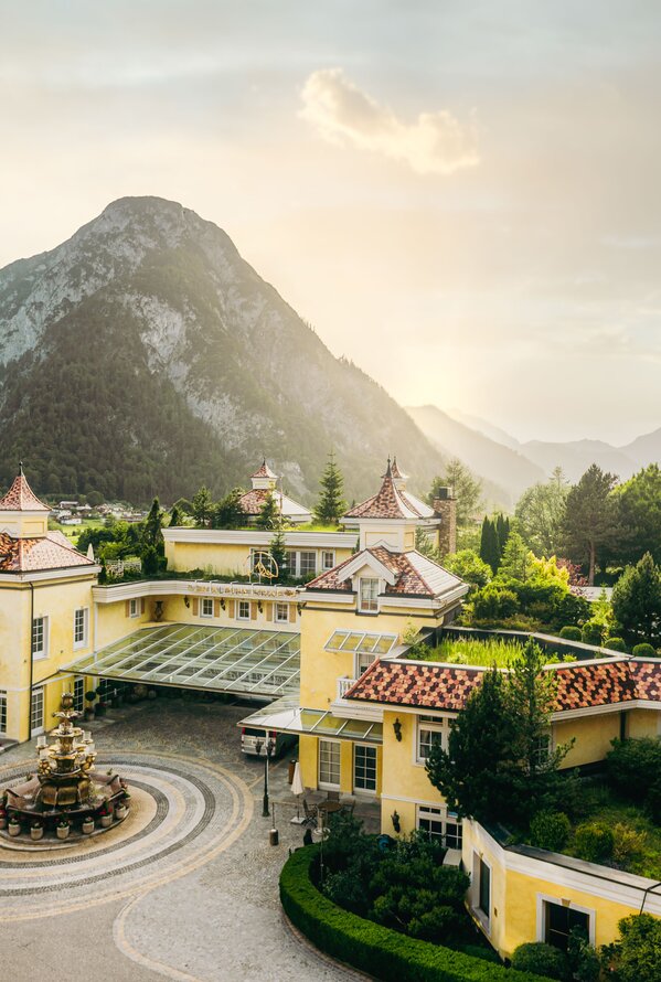 Elegante Hotelanlage mit Brunnen, alpiner Architektur und Bergpanorama im Abendlicht