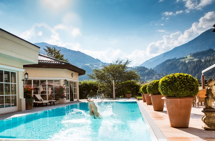 Person springt in Pool vor Bergkulisse