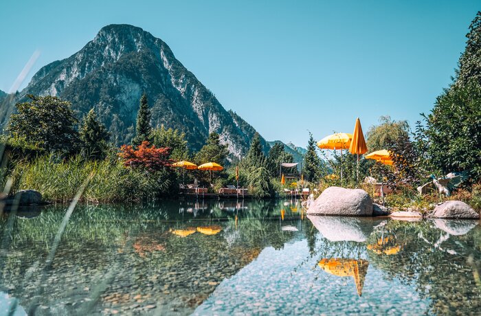 Bergsee mit gelben Sonnenschirmen und Spiegelung im Wasser vor Bergkulisse