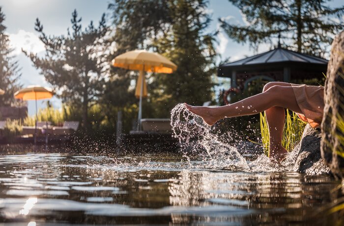 Beine im Wasser, Spritzer, gelber Sonnenschirm und Pavillon im Hintergrund