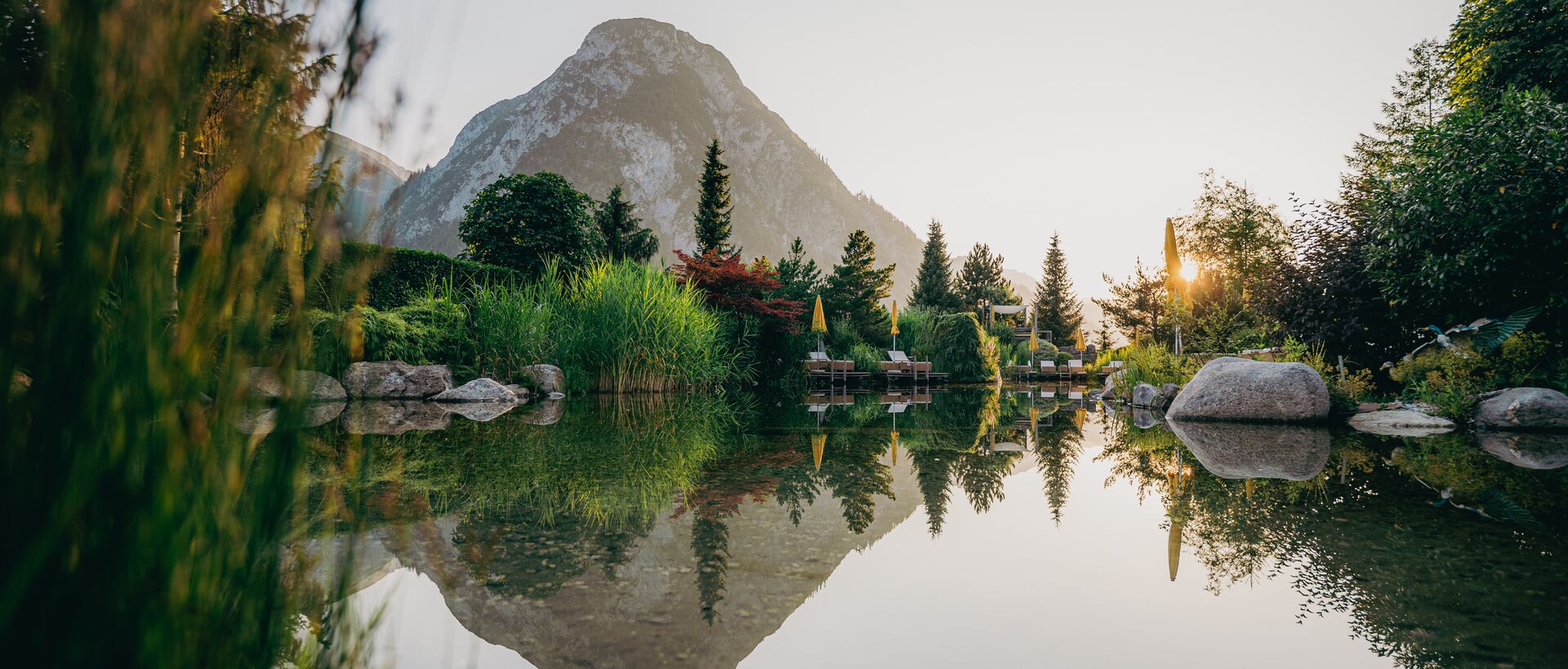 Idyllic natural swimming pond with mountain panorama and reflection at sunset