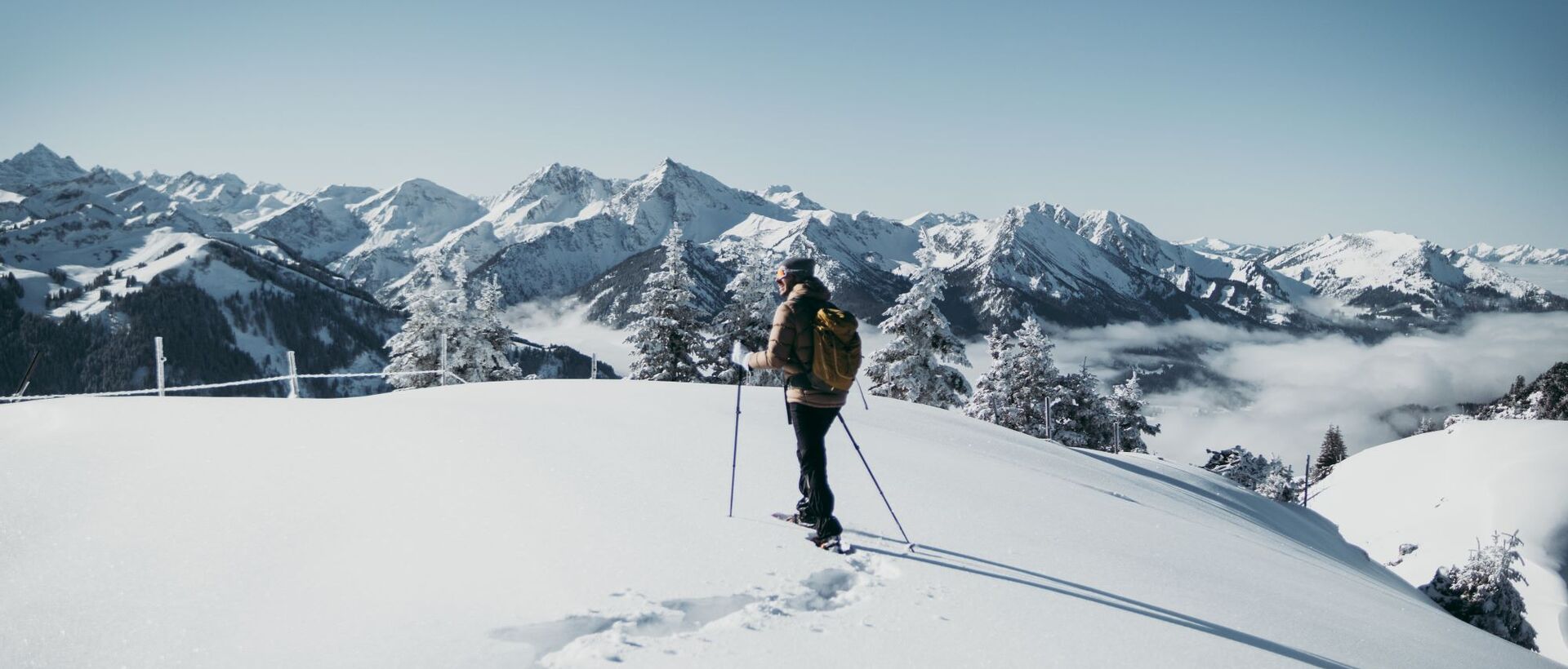 Hiker with backpack and poles in the snow in front of mountain panorama