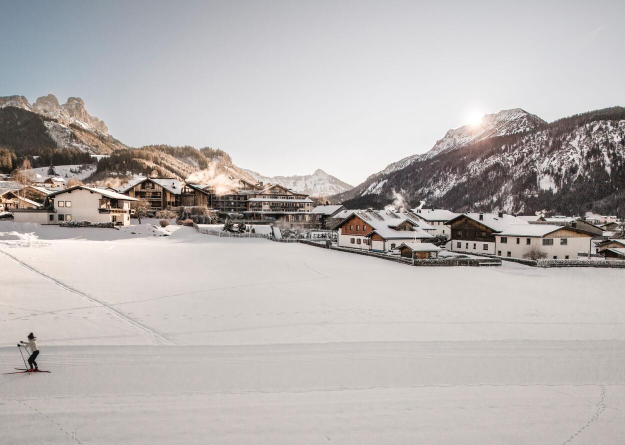 Verschneite Berglandschaft mit kleinen Häusern und einer einzelnen Person auf Langlaufskiern.