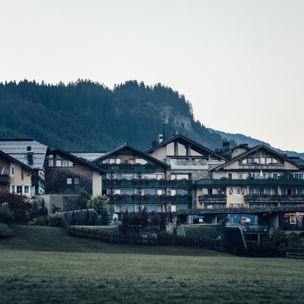 Hotel complex in front of a wooded mountain under a bright sky