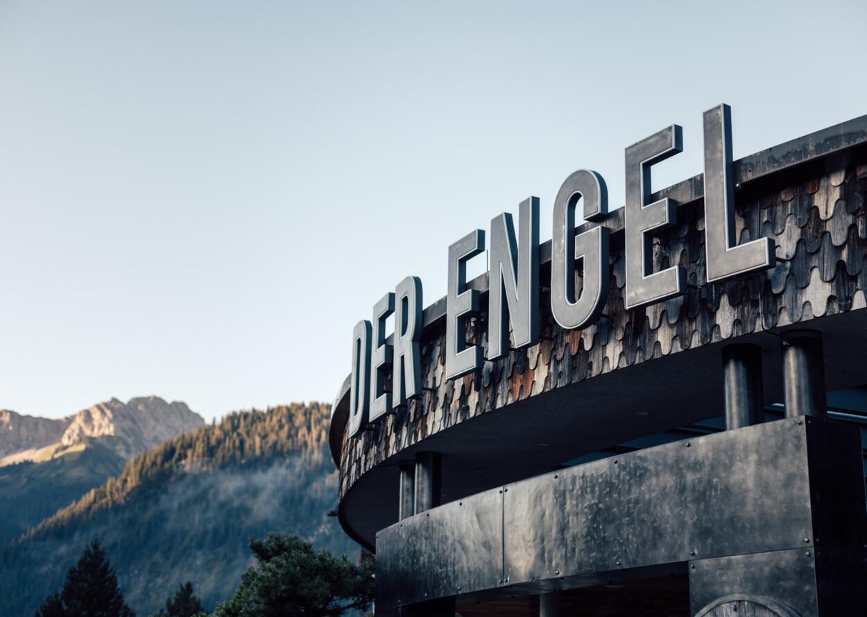 Exterior view of the Hotel "Der Engel" with large lettering against a mountain backdrop