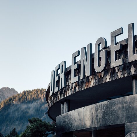 Exterior view of the Hotel "Der Engel" with large lettering against a mountain backdrop
