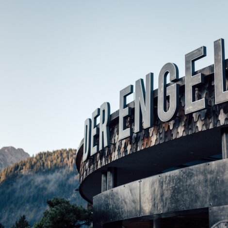 Exterior view of the Hotel "Der Engel" with large lettering against a mountain backdrop