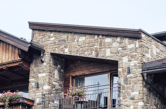Hausfassade mit Steinmauerwerk und Balkon unter grauem Himmel