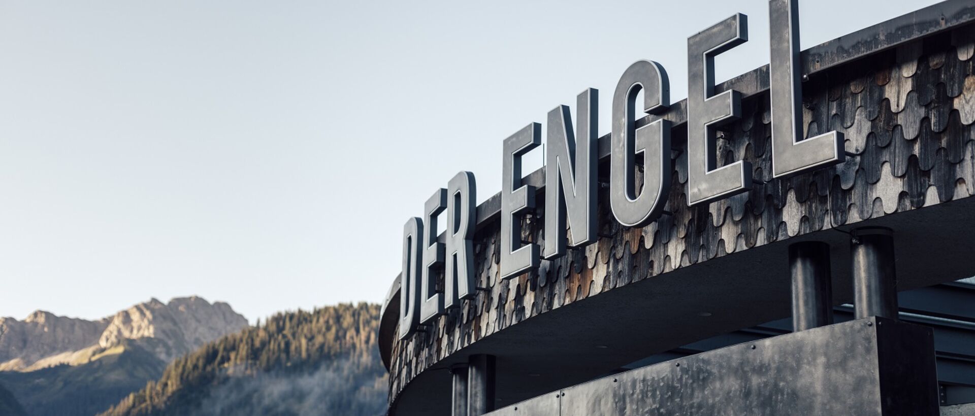 Gebäude mit der Aufschrift DER ENGEL vor Bergkulisse