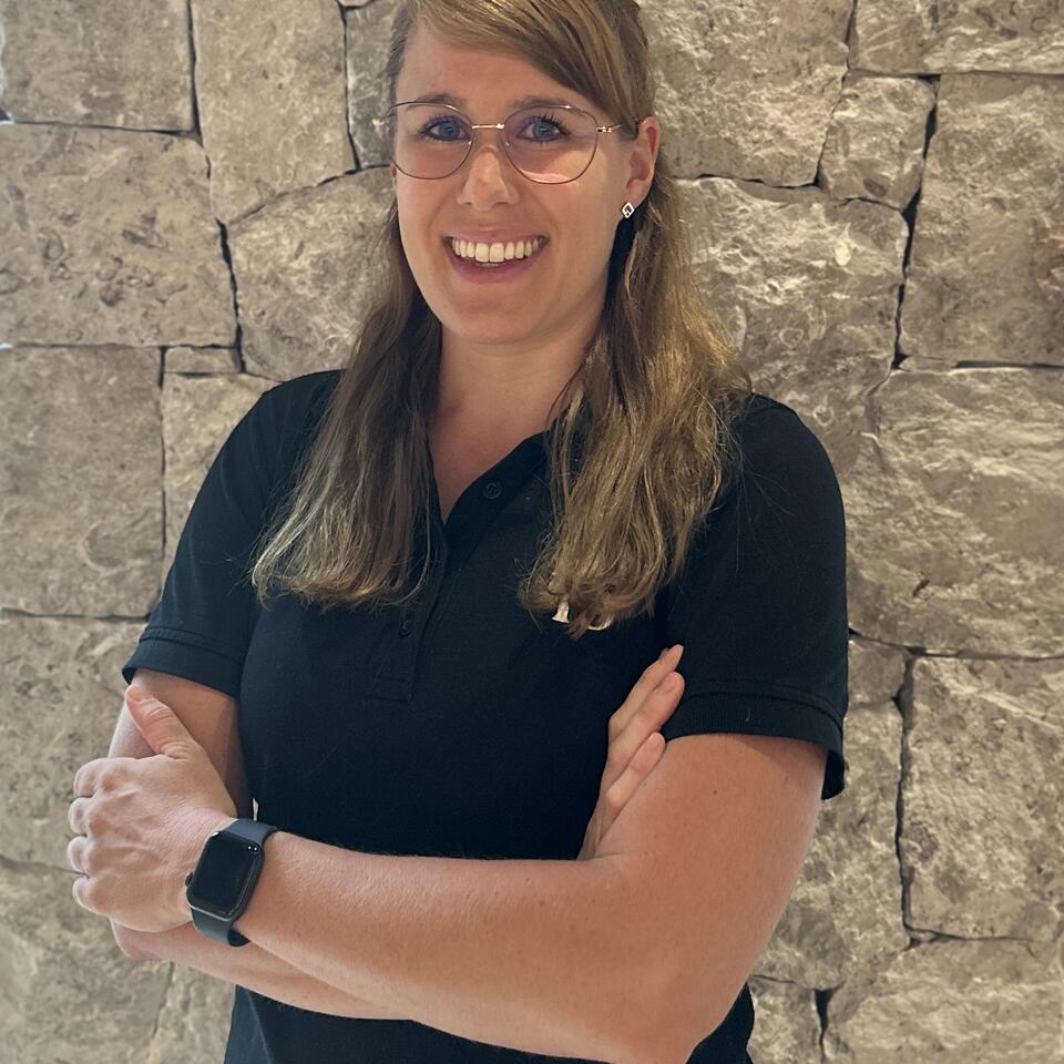 Woman with glasses smiling in front of a stone wall