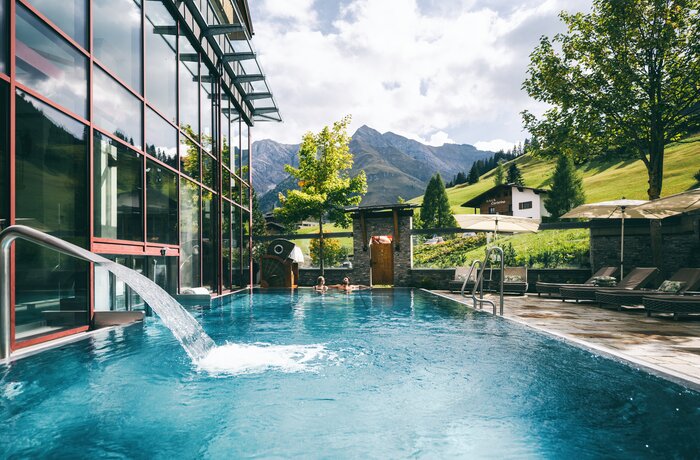 Schwimmbad vor Bergkulisse mit Glasfassade und Wasserfall im Warther Hof