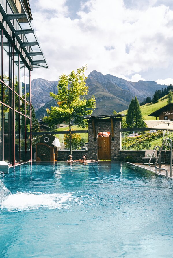 Schwimmbad vor Bergkulisse mit Glasfassade und Wasserfall im Warther Hof