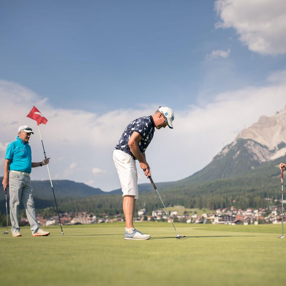 Golfer beim Putten auf einem Golfplatz mit Bergpanorama