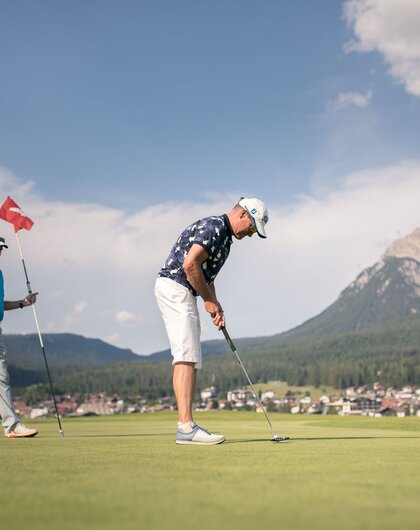 Golfer beim Putten auf einem Golfplatz mit Bergpanorama
