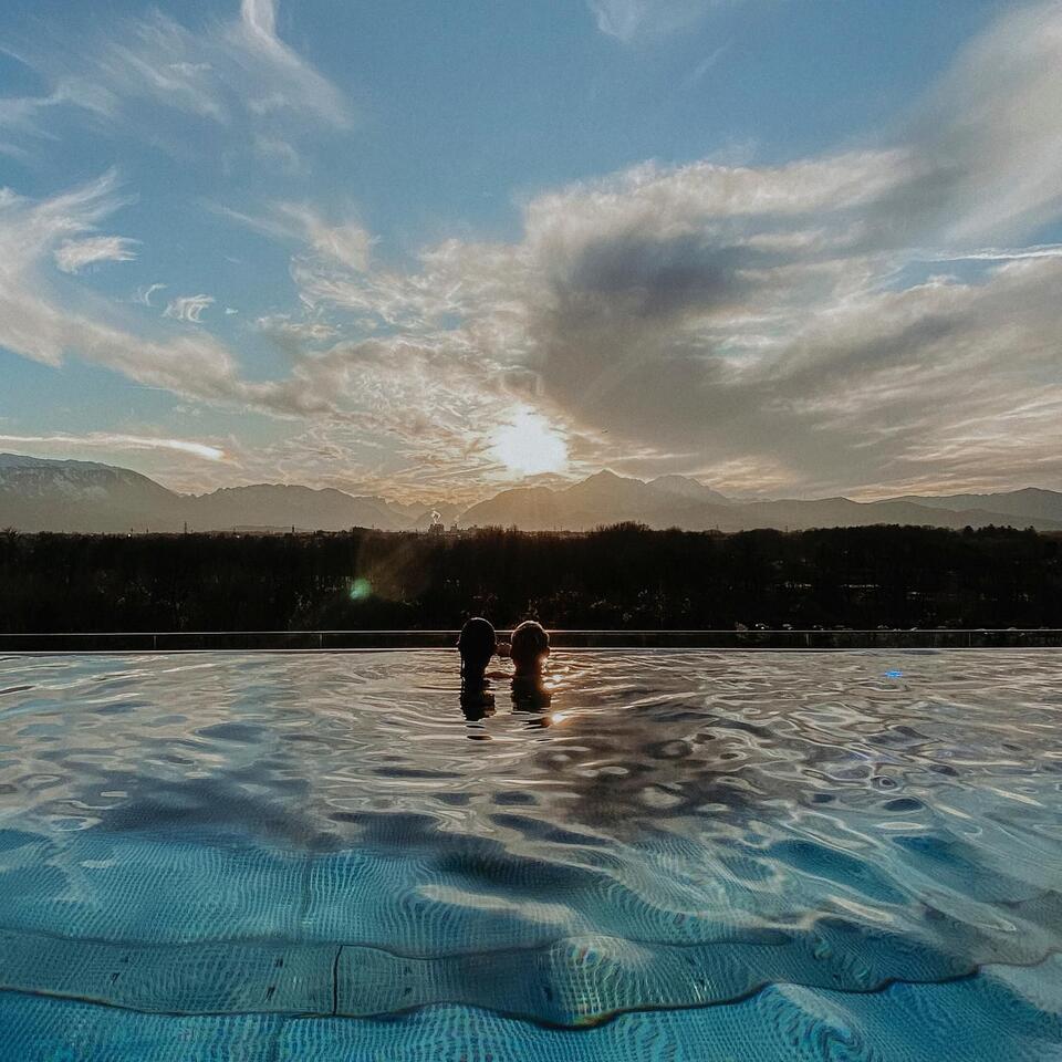 Zwei Personen im Pool vor Bergpanorama und Sonnenuntergang