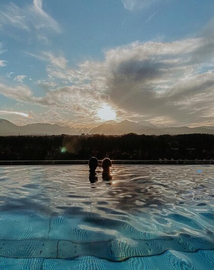 Zwei Personen im Pool vor Bergpanorama und Sonnenuntergang