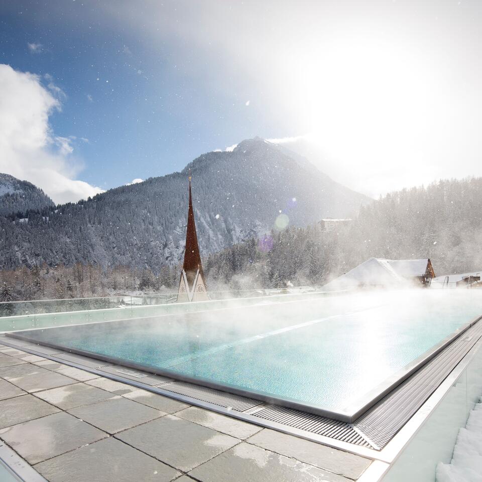 Winterlicher Außenpool mit Dampf, schneebedeckte Berge im Hintergrund