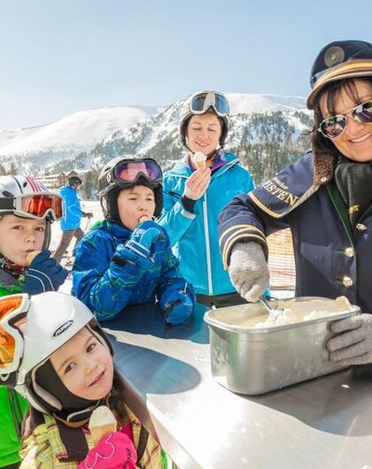 Woman sells ice cream to children in ski clothes against a mountain backdrop