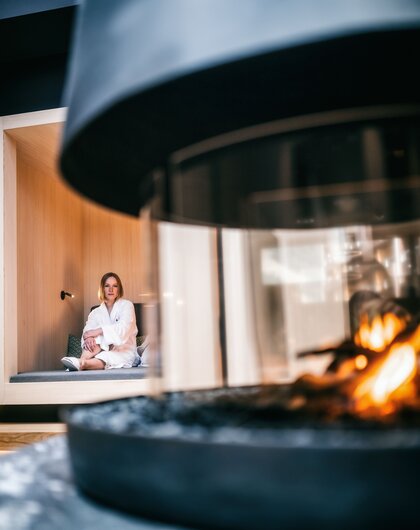 Woman in bathrobe sitting in niche, fireplace in foreground