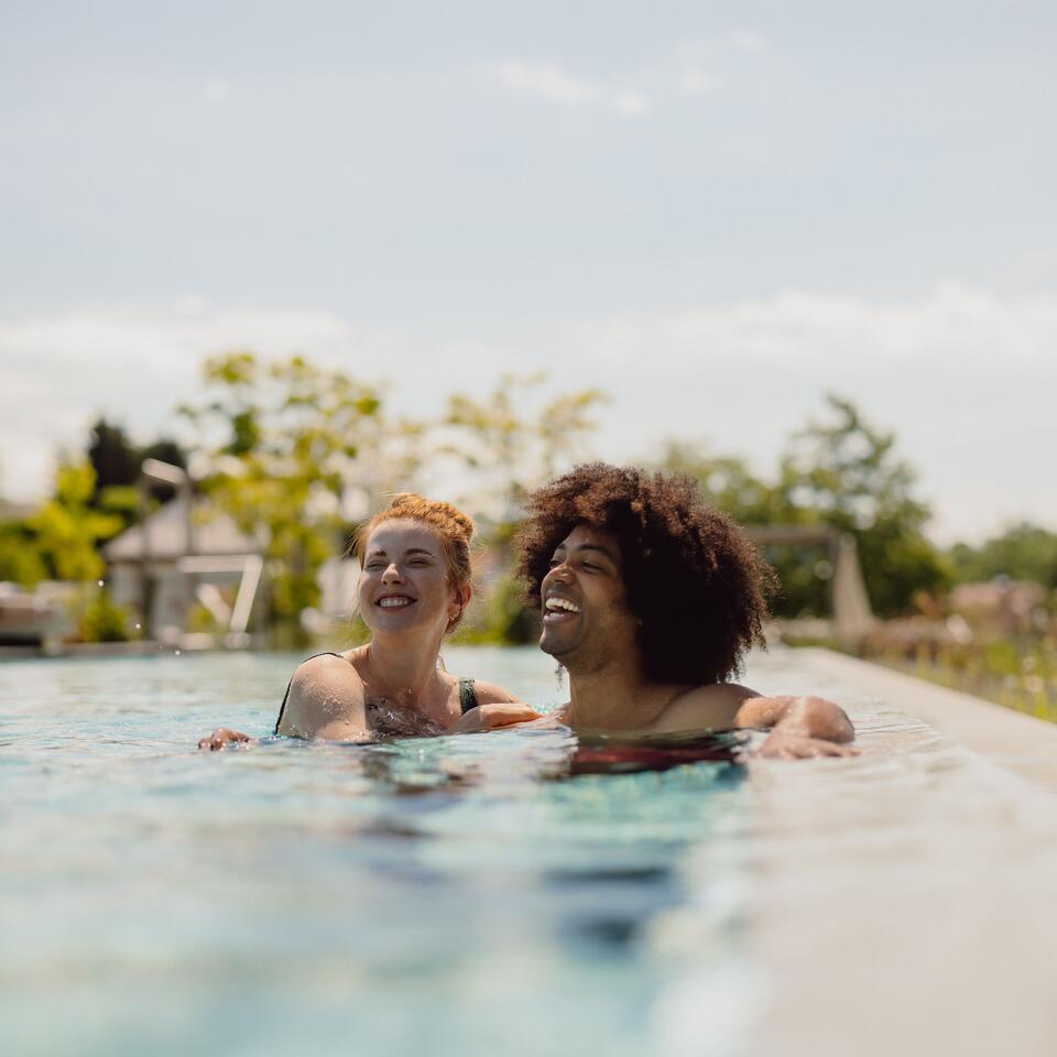 Zwei lachende Personen schwimmen in einem Pool