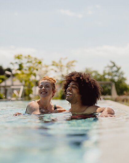 Zwei lachende Personen schwimmen in einem Pool