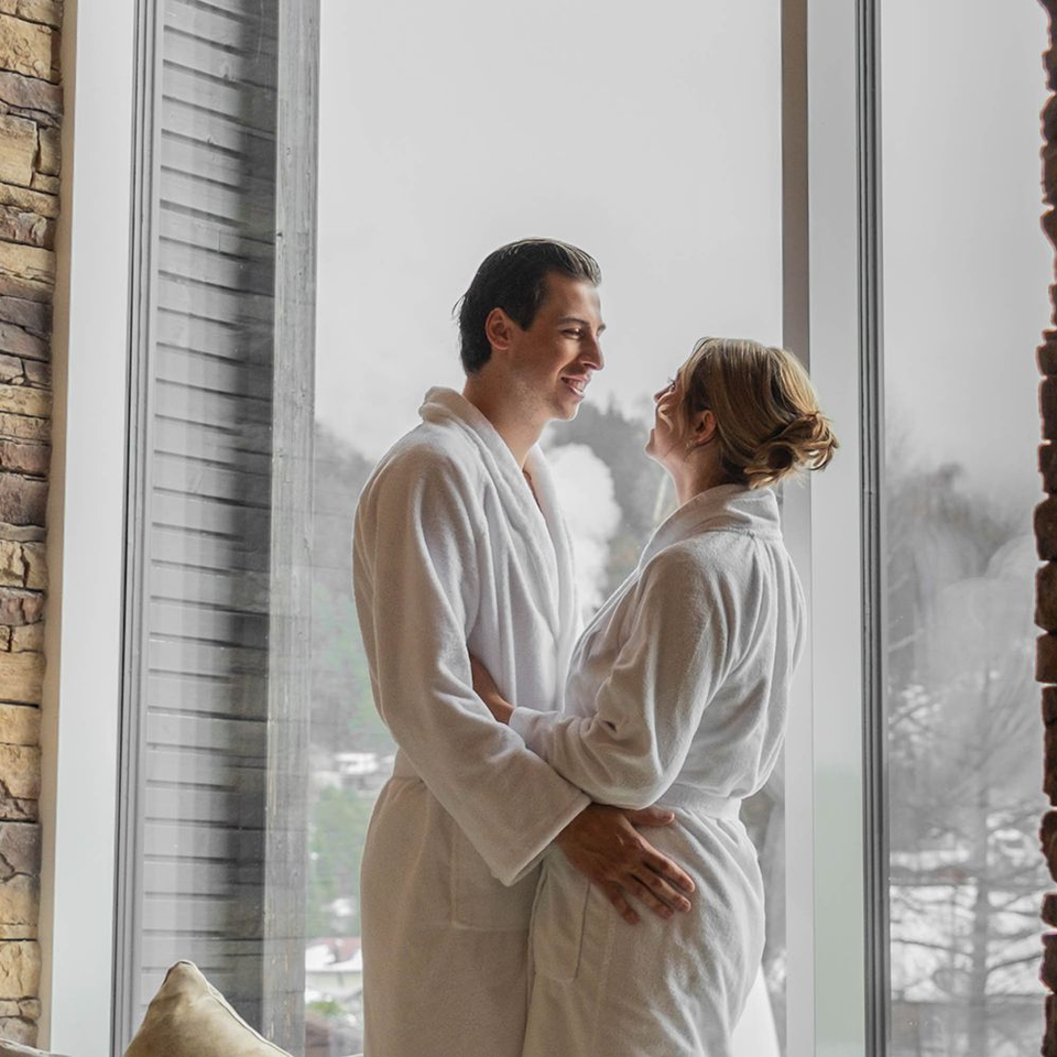 Paar in Bademänteln umarmt sich vor Fenster