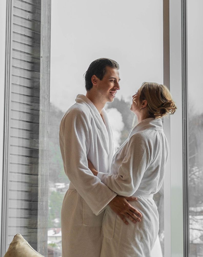 Couple in bathrobes hugging in front of window