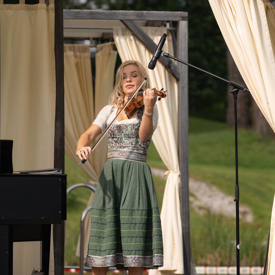 Blonde Frau im Dirndl spielt Geige auf einer Bühne