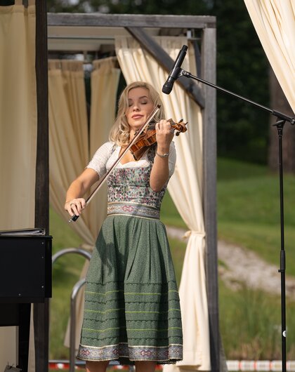 Blonde Frau im Dirndl spielt Geige auf einer Bühne