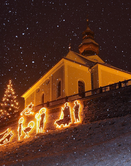 Kirche mit Weihnachtsbeleuchtung und Krippendarstellung im Schnee unter Sternenhimmel