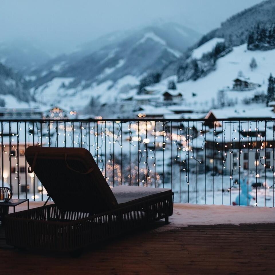 Liege auf Balkon mit Blick auf verschneite Berge und Lichter einer Stadt im Tal
