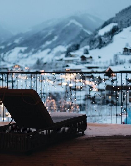 Liege auf Balkon mit Blick auf verschneite Berge und Lichter einer Stadt im Tal