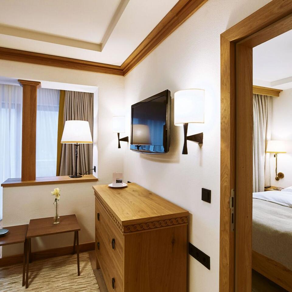 Hotelzimmer mit Kommode, Fernseher und Blick ins Schlafzimmer