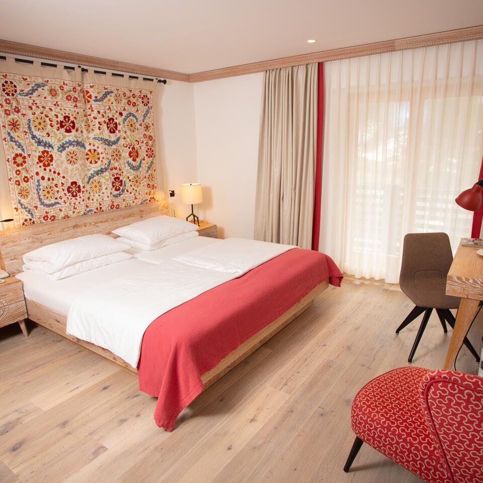 Schlafzimmer mit Doppelbett, gemusterter Wandteppich, Schreibtisch und Stuhl in hellem Holzdesign