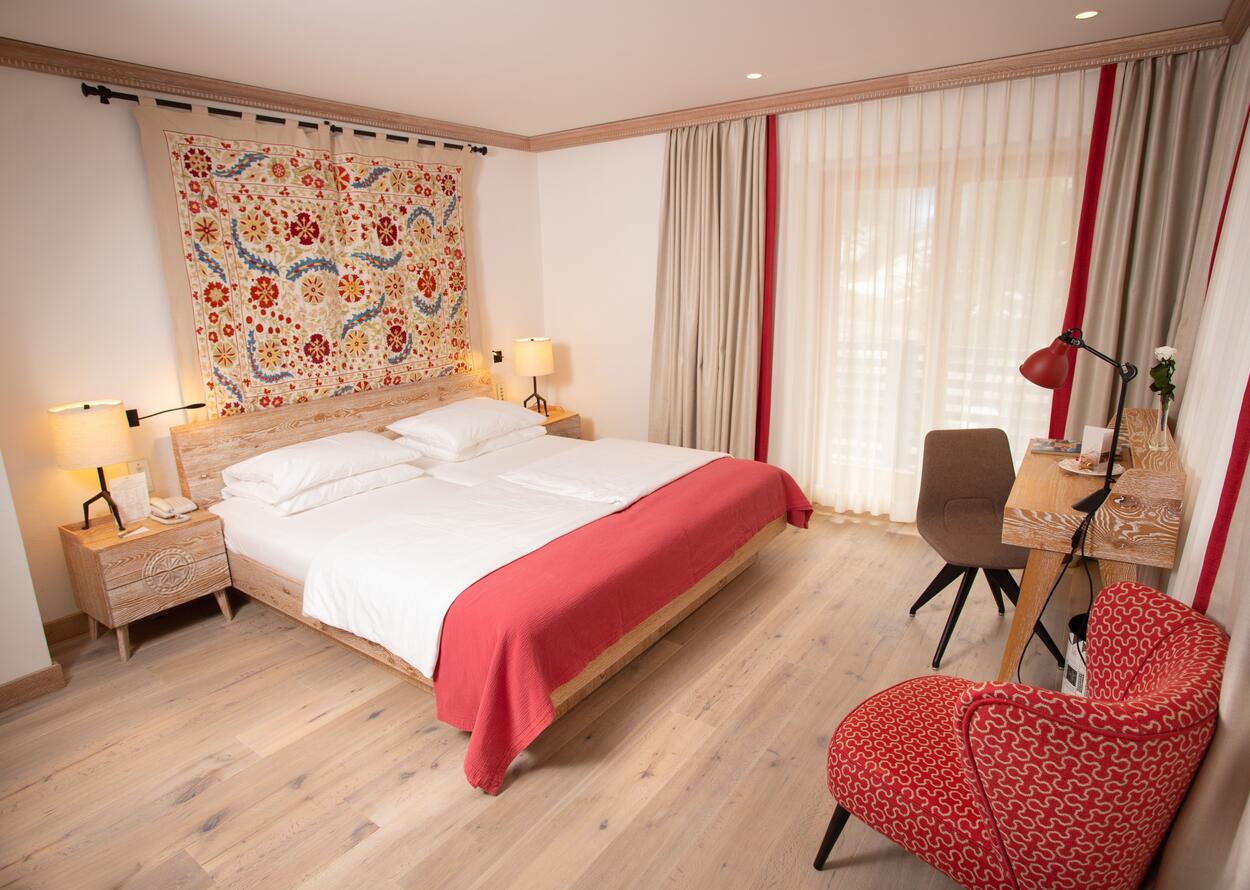 Bedroom with double bed, patterned tapestry, desk and chair in light wood design