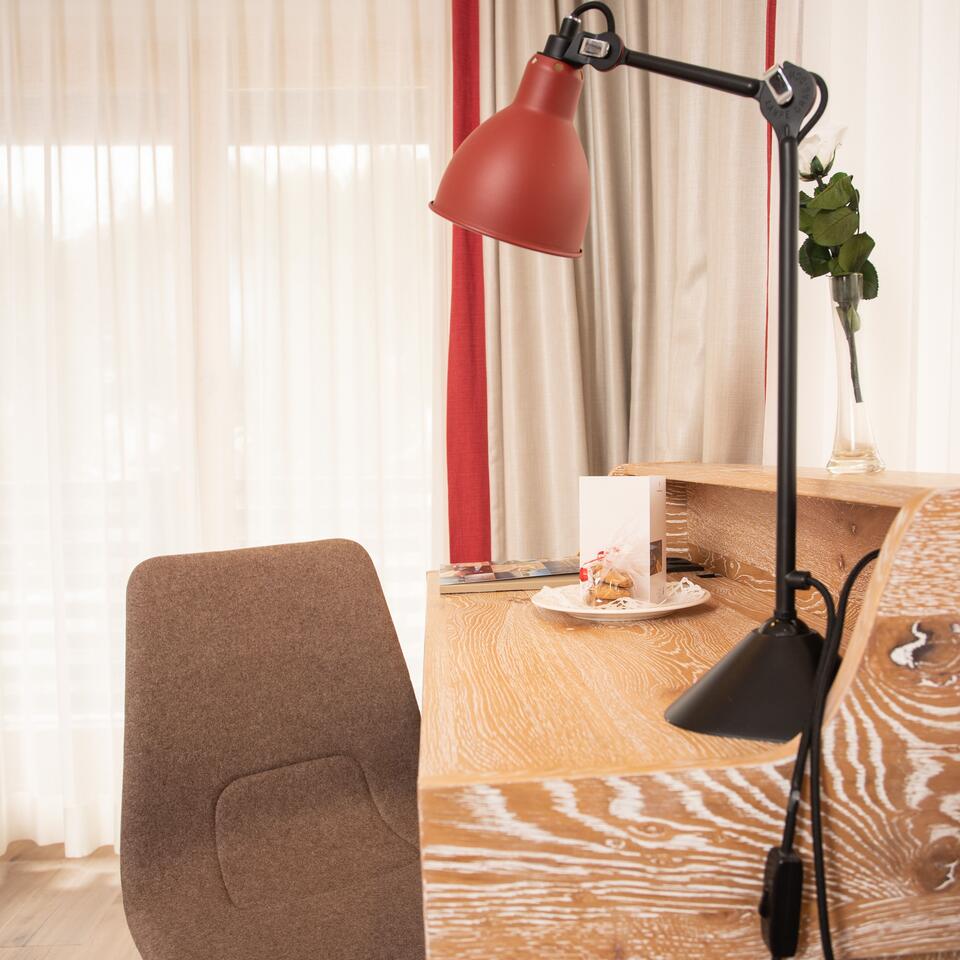 Schreibtisch mit roter Lampe, Stuhl und Dekoration vor Fenster