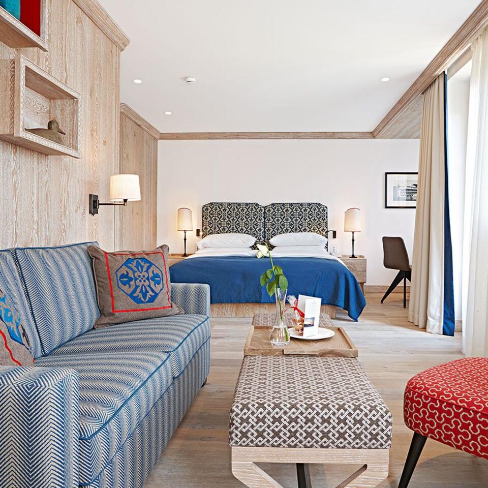 Hotelzimmer mit blauem Bett, Sofa, Sessel und Holzboden